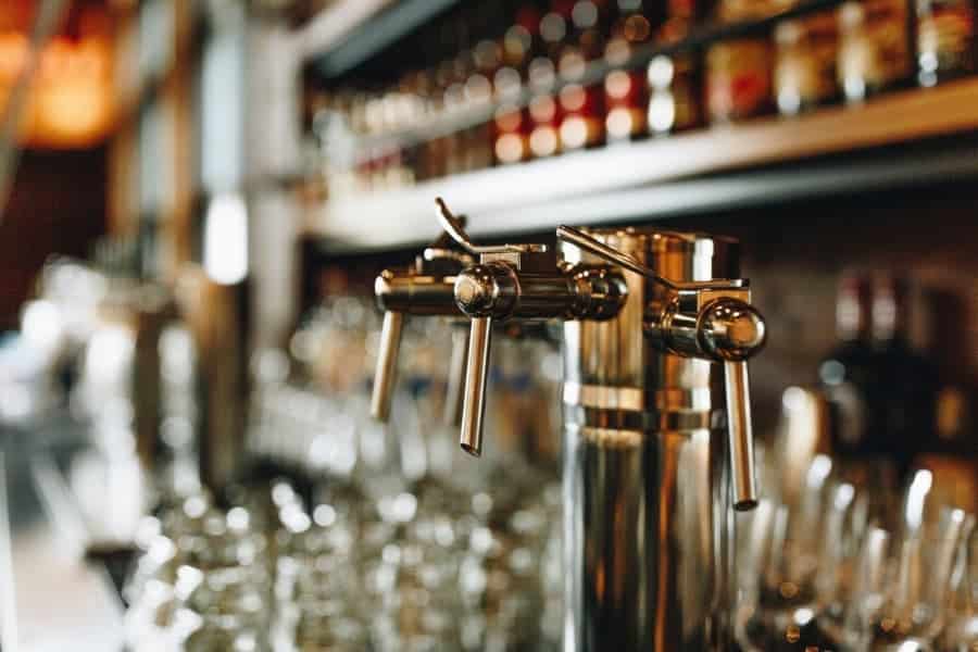 Silver direct draw beverage system sitting on bar with glassware and bottles of alcohol in background