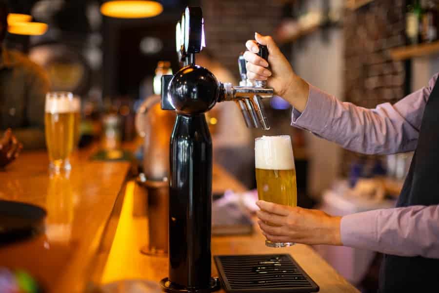 Person pouring beer from tap into glass in pub